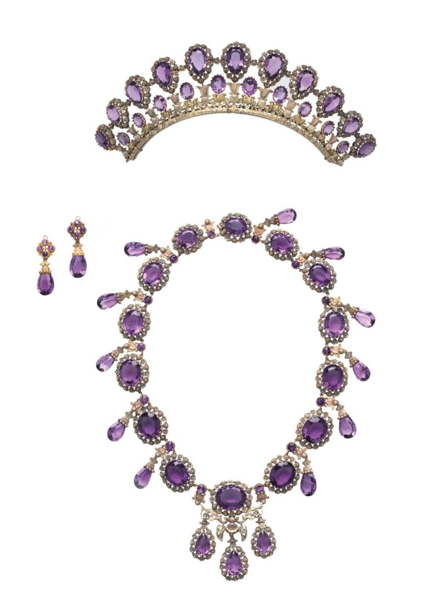 Gold jewelry set with amethyst stones, including a tiara, necklace, and earrings, elegantly arranged on a white background.