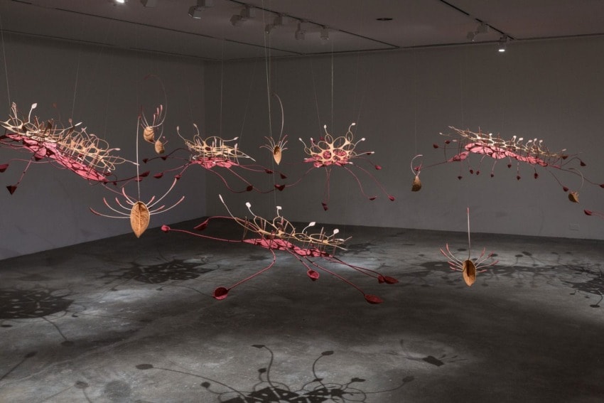 Hanging abstract sculptures in a gallery with intricate designs and shadows on the floor.