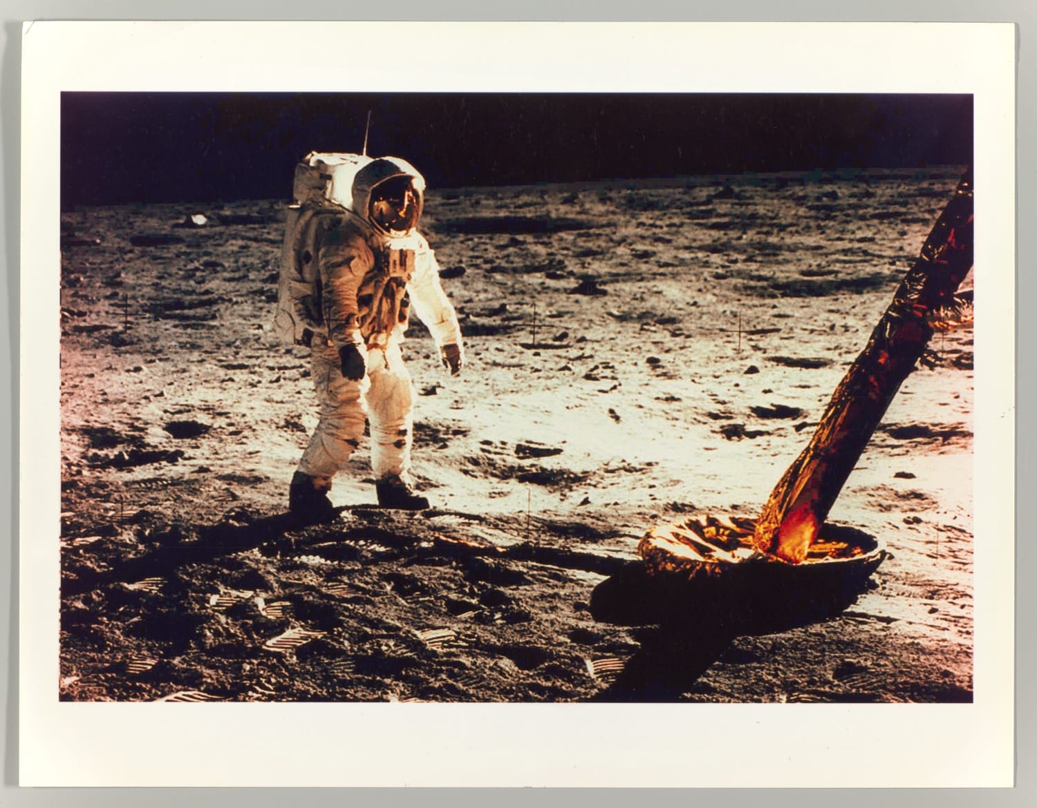 Astronaut in a spacesuit walking on the moon near a spacecraft part on the lunar surface.