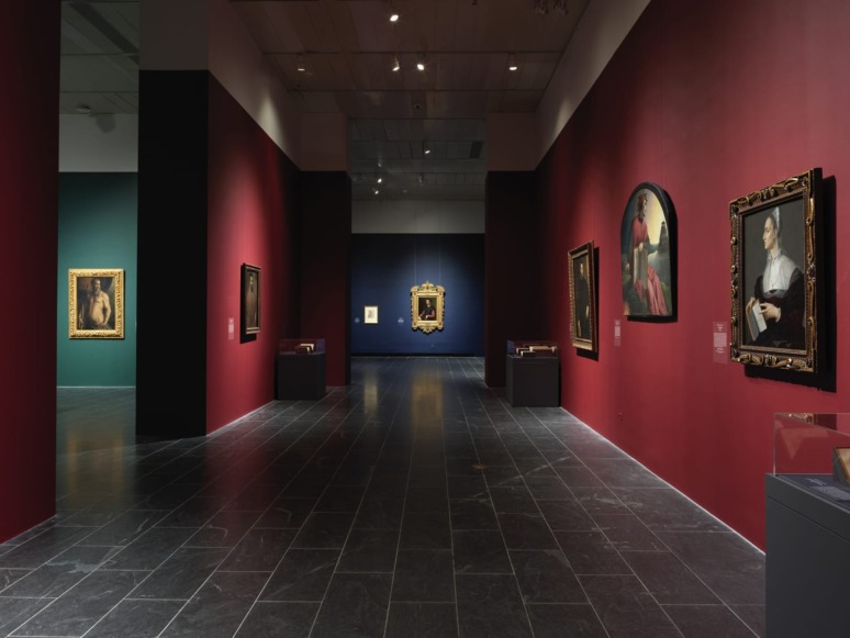 Museum gallery with paintings displayed on red and green walls, dim lighting enhances the artwork's visibility.