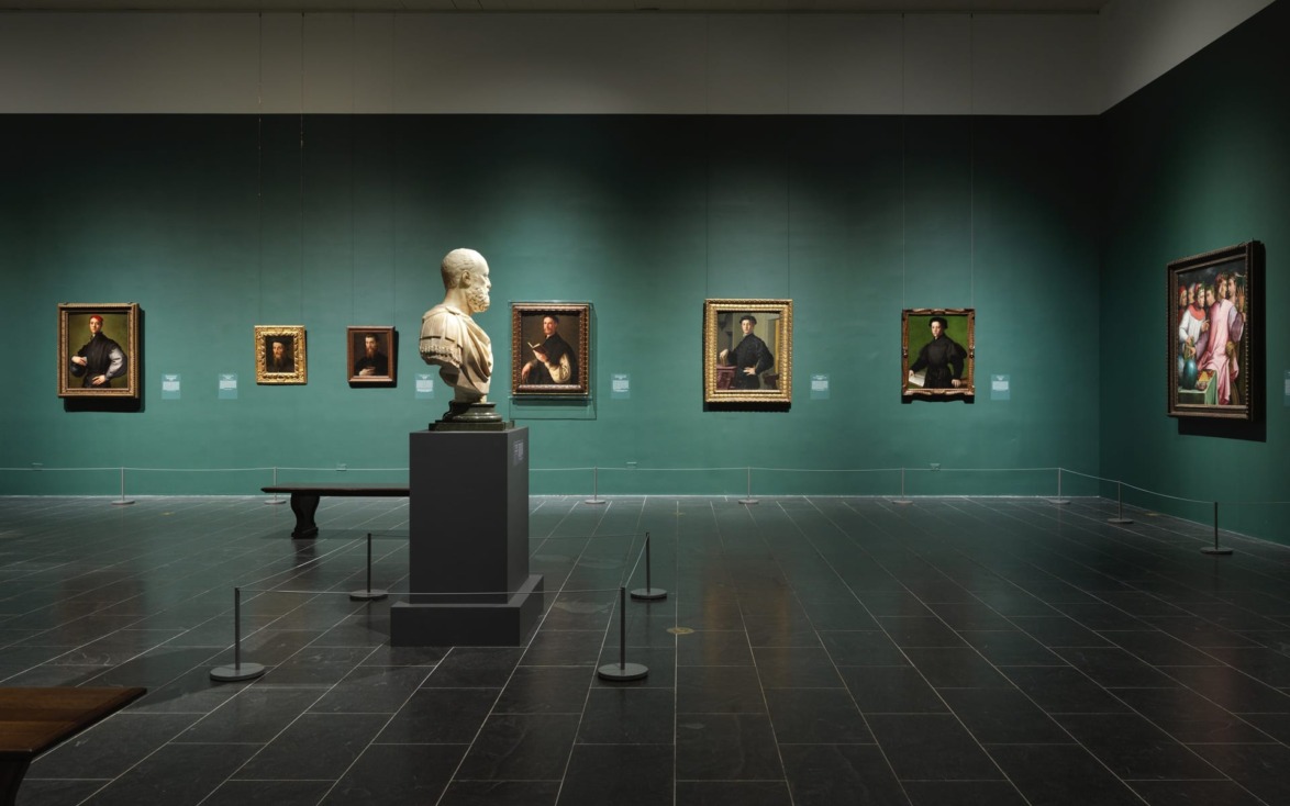 Art gallery interior with a marble bust and framed paintings on a green wall, dark tiled floor, and minimal lighting.