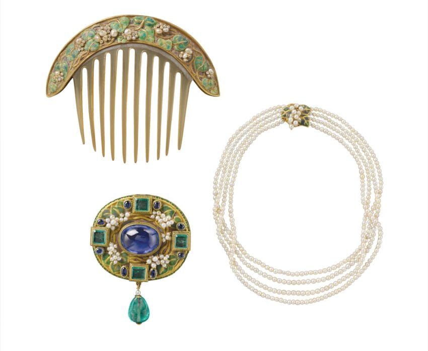 Antique jewelry set with pearl necklace, gold comb with green enamel, and jeweled brooch with blue and green stones.