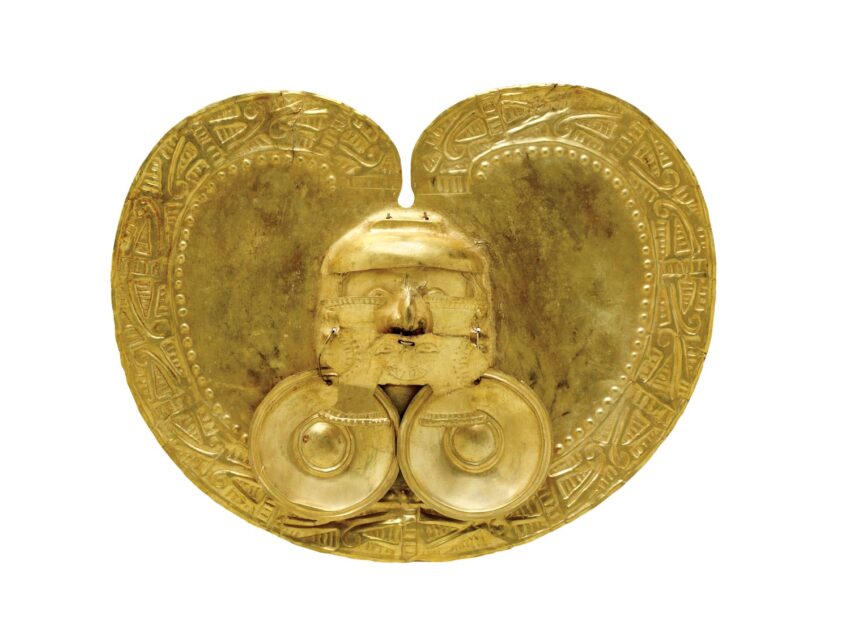 Golden artifact with intricate patterns and a central face from the Calima culture on a white background.