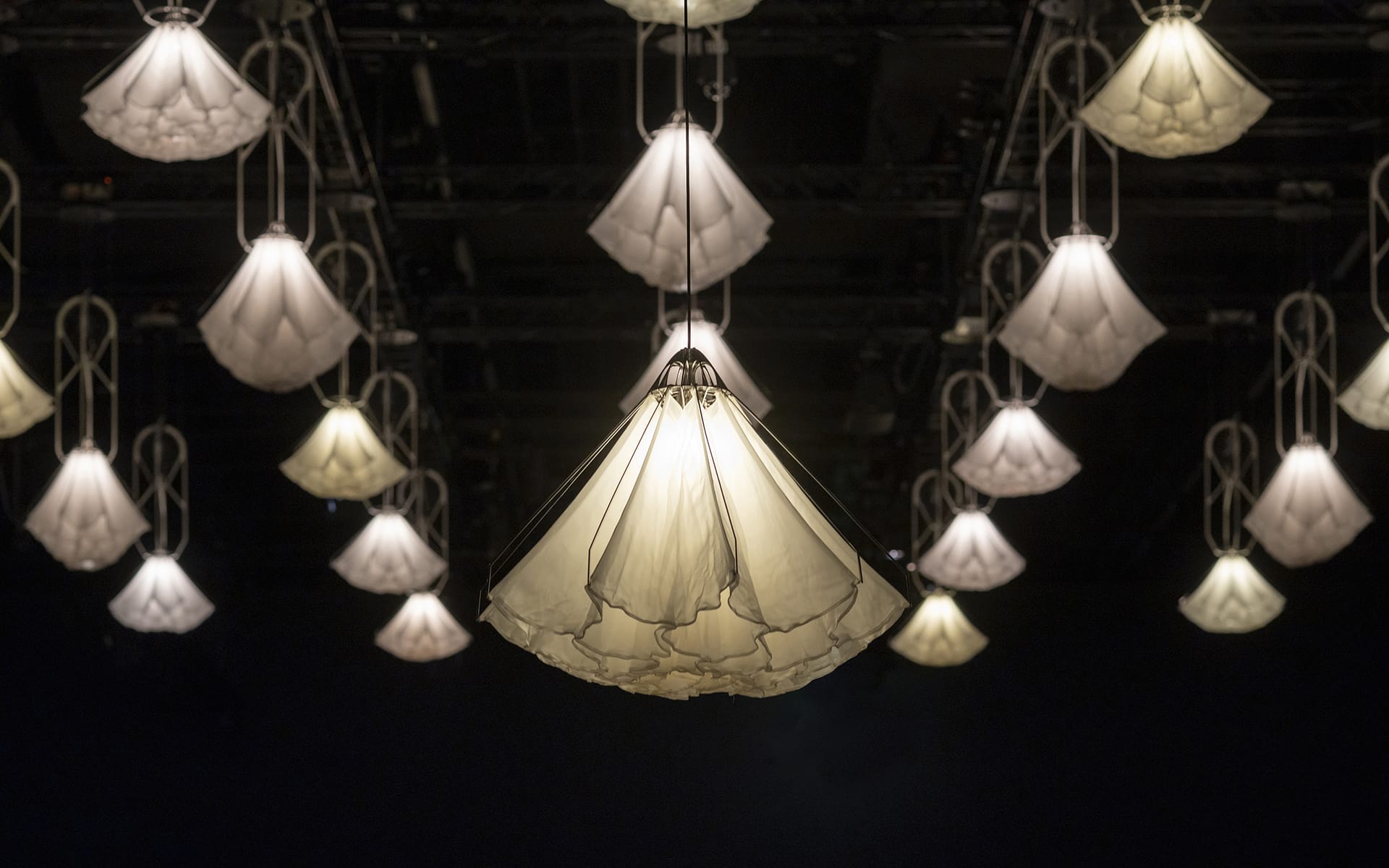 Hanging cluster of soft glow pendant lights with umbrella-like design, creating a warm, elegant atmosphere against a dark background.