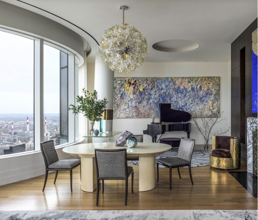 Modern dining room with a round table, elegant chairs, art on the wall, a grand piano, large window, and cityscape view.