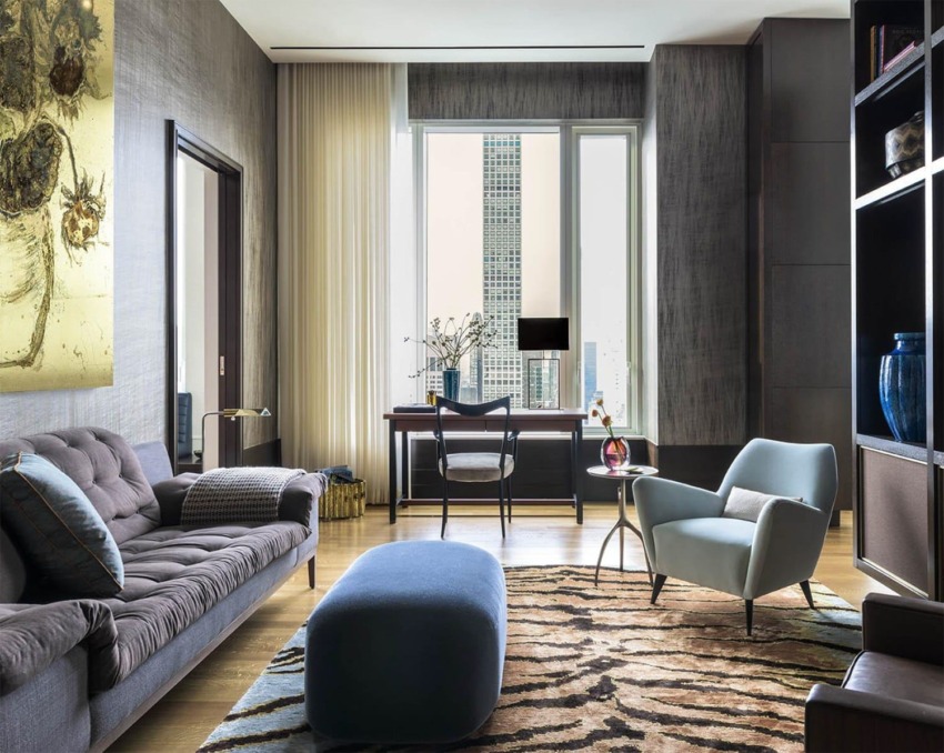 Modern living room with a gray sofa, blue armchairs, zebra-pattern rug, and large window overlooking cityscape.