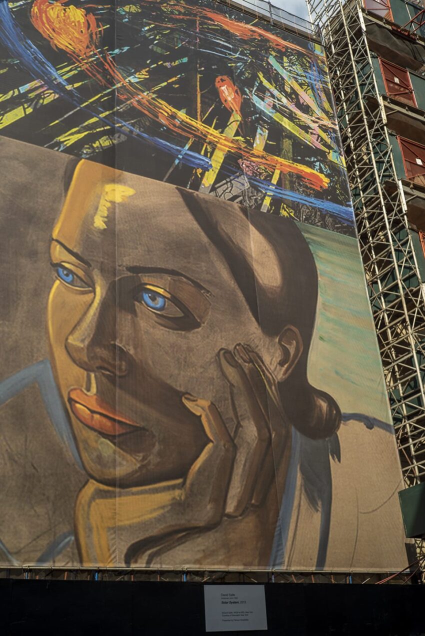 Scaffold with colorful mural of abstract art and portrait of a woman with blue eyes, hand resting on her cheek.