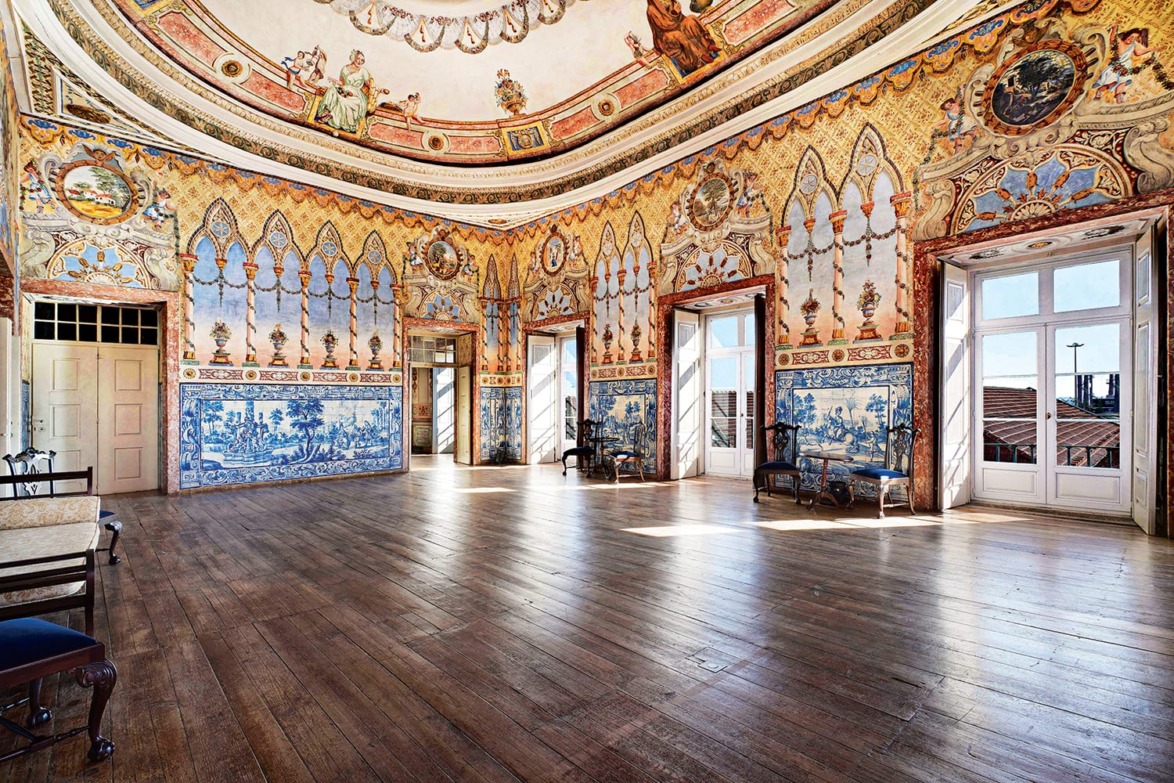 Ornate historic room with decorative frescoed ceiling, wood floors, large windows, and intricate wall designs.