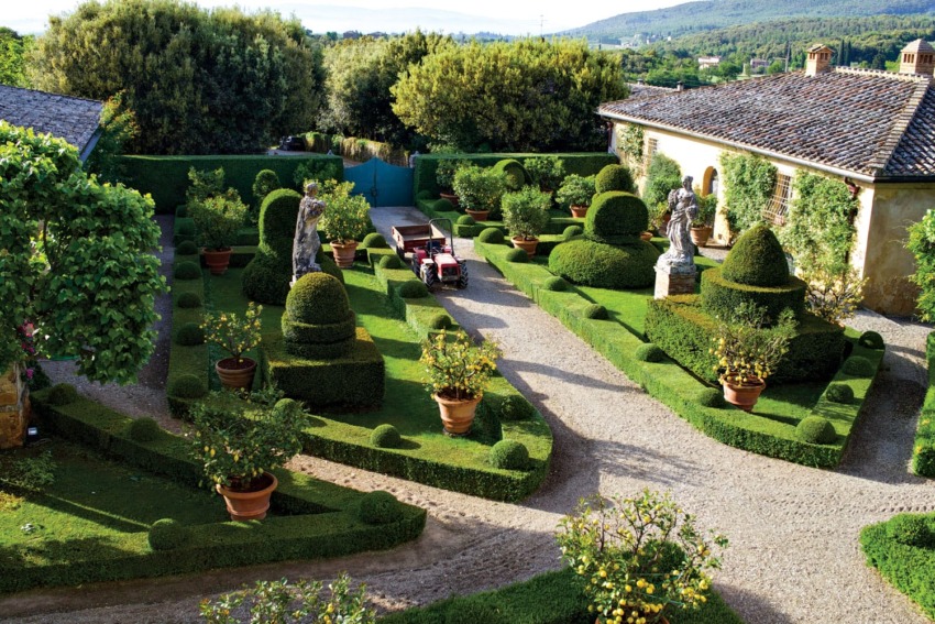Beautiful garden with manicured hedges, topiary sculptures, potted plants, and a gravel path in an elegant courtyard setting.