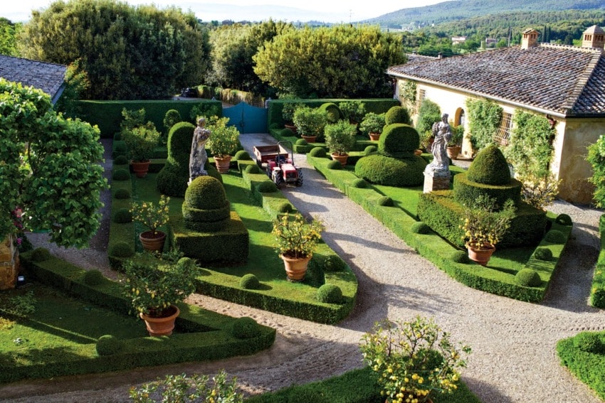 Beautiful garden with manicured hedges, topiary sculptures, potted plants, and a gravel path in an elegant courtyard setting.