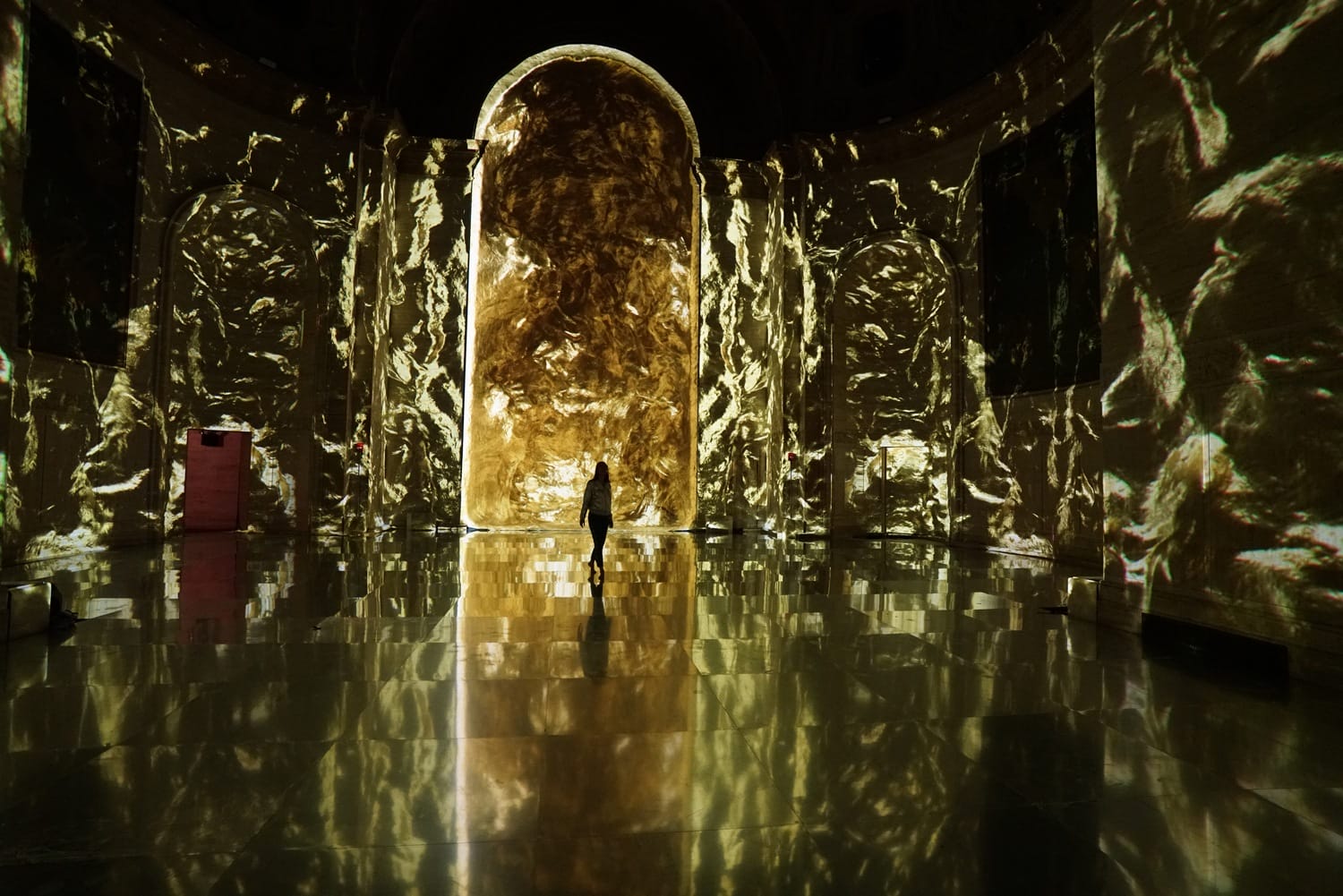 Person standing in illuminated room with golden light projections on walls and floor.