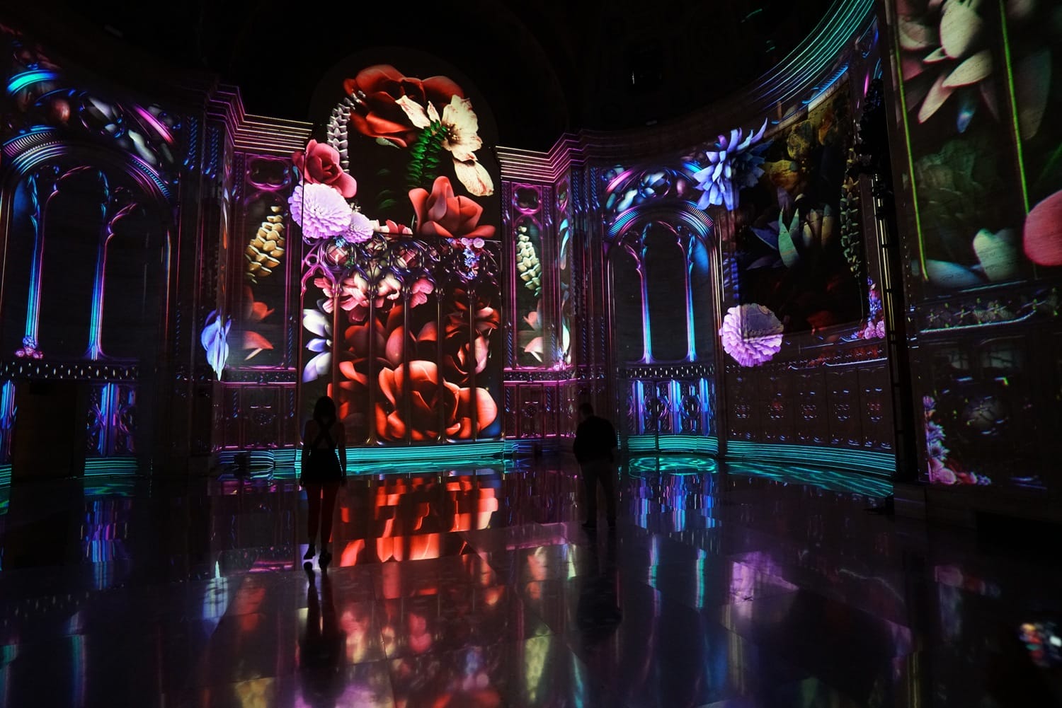 Colorful digital art projections on large screen with floral patterns in a dark room, reflecting on glossy floor.
