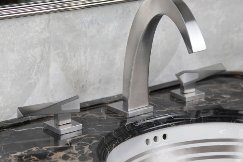 Modern bathroom sink with sleek, silver faucet set on a polished black marble countertop in front of a wall mirror.