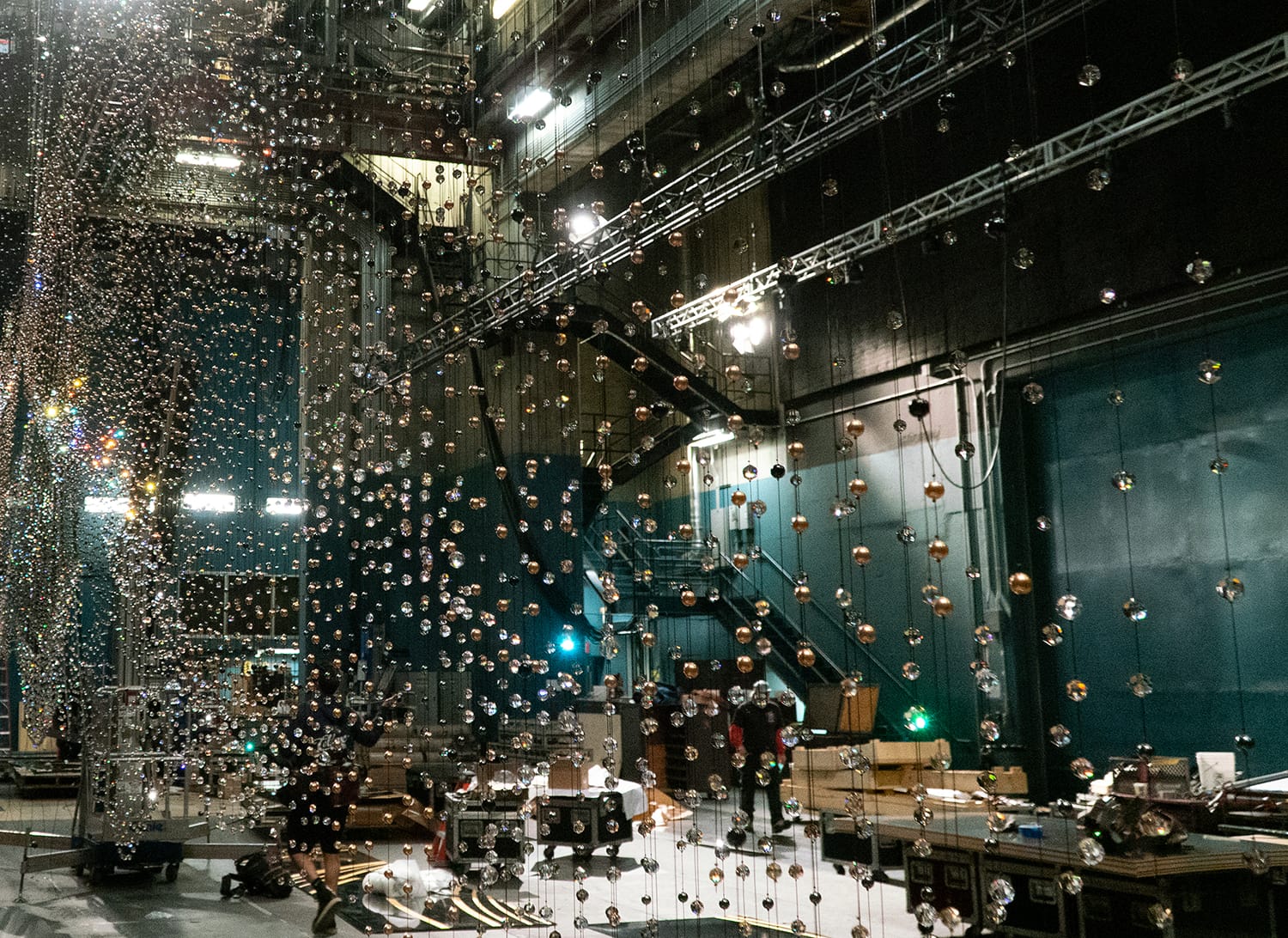 Stage with suspended glass spheres, lit atmosphere, and backstage equipment visible in an artistic and creative setting.