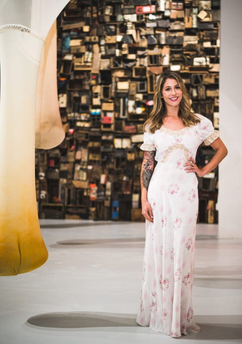 Woman in a floral dress standing in an art gallery with eclectic wall display in the background