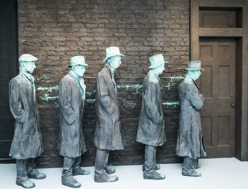 Bronze statues of men in line against a brick wall, depicting a historical scene of waiting during the Great Depression.
