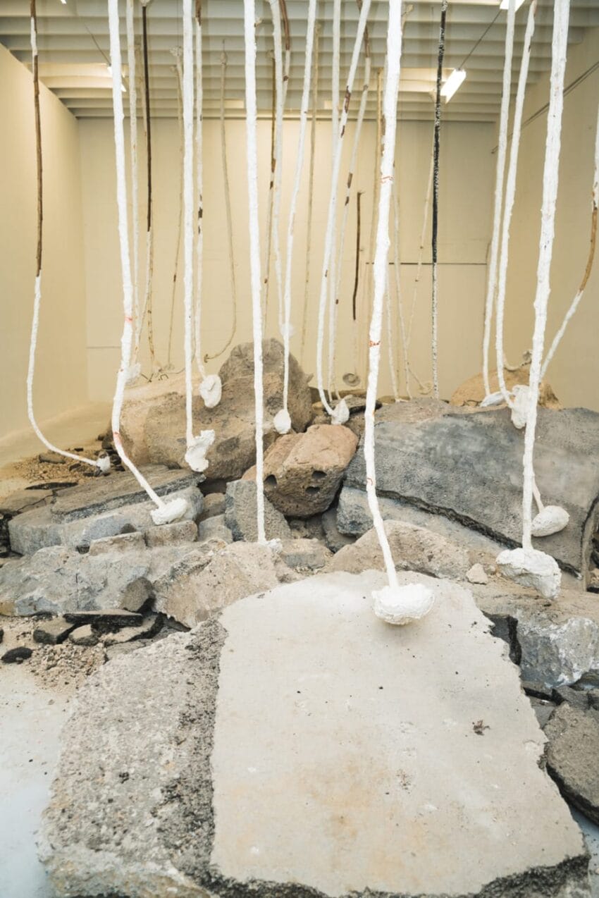 Concrete slabs with white strings hanging from the ceiling in a modern art installation in a gallery space.
