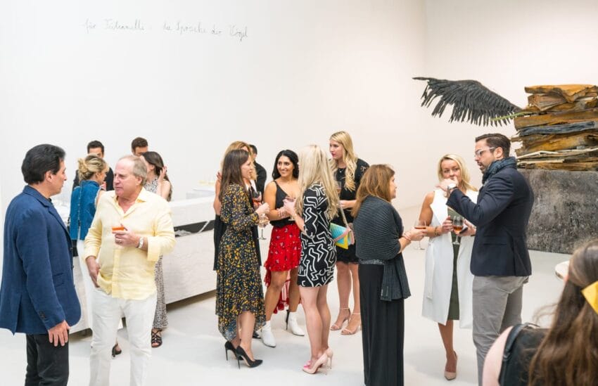 People socializing at an art gallery event with sculptures and wall writing in the background.