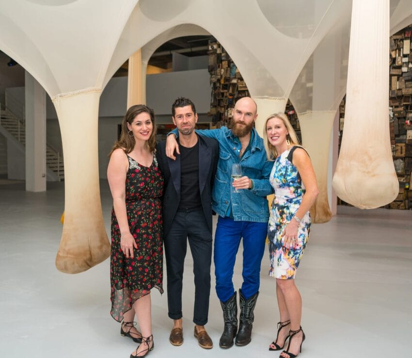 Four people standing together in a modern art gallery, with sculptures and artworks in the background.