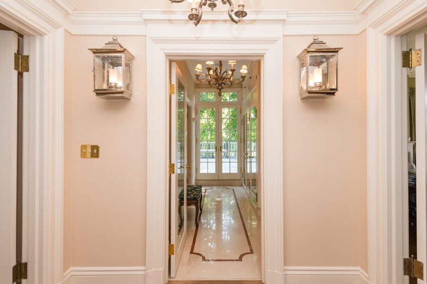 Elegant hallway with chandeliers, wall sconces, and large windows at the end, allowing natural light to stream in.