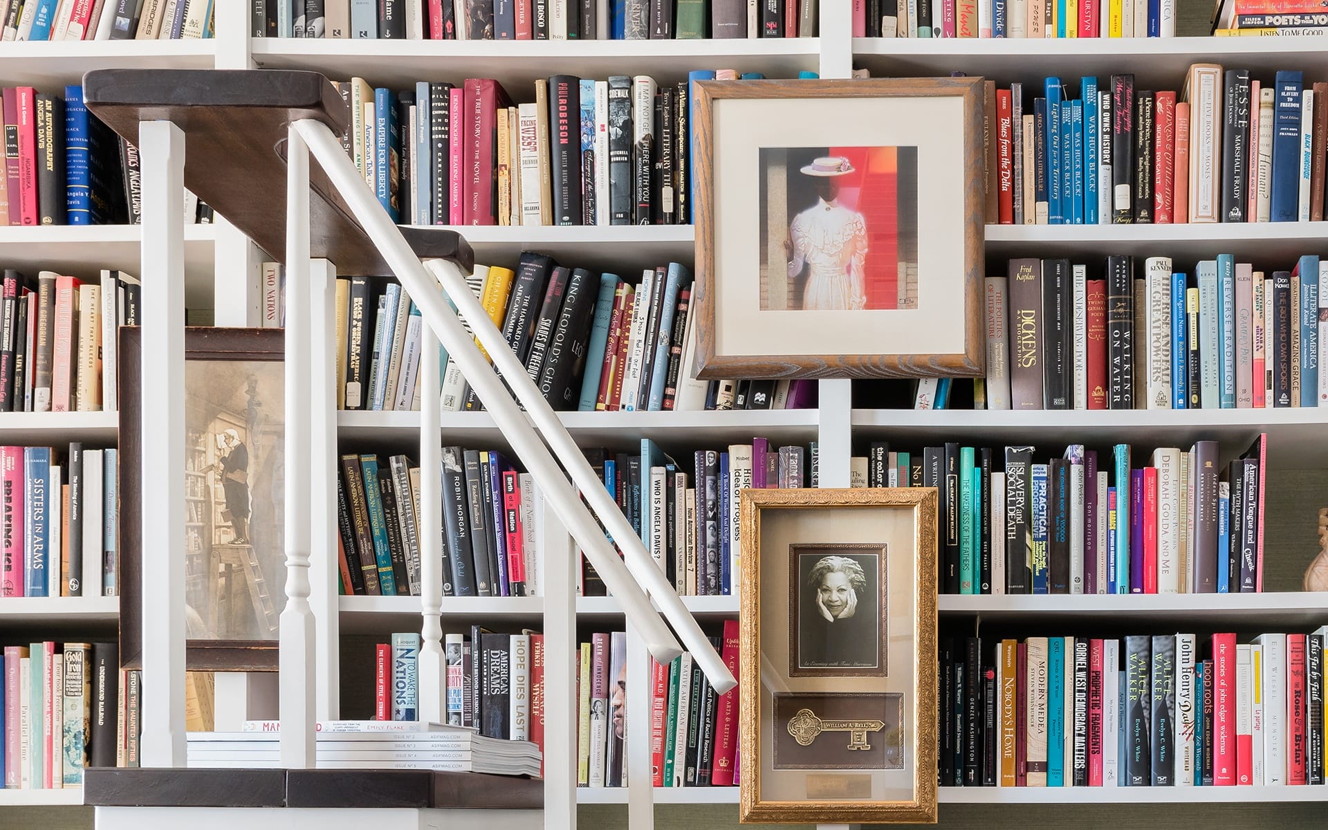 Bookshelf filled with colorful books, framed pictures, and decorative items on a wooden staircase in a cozy reading space.