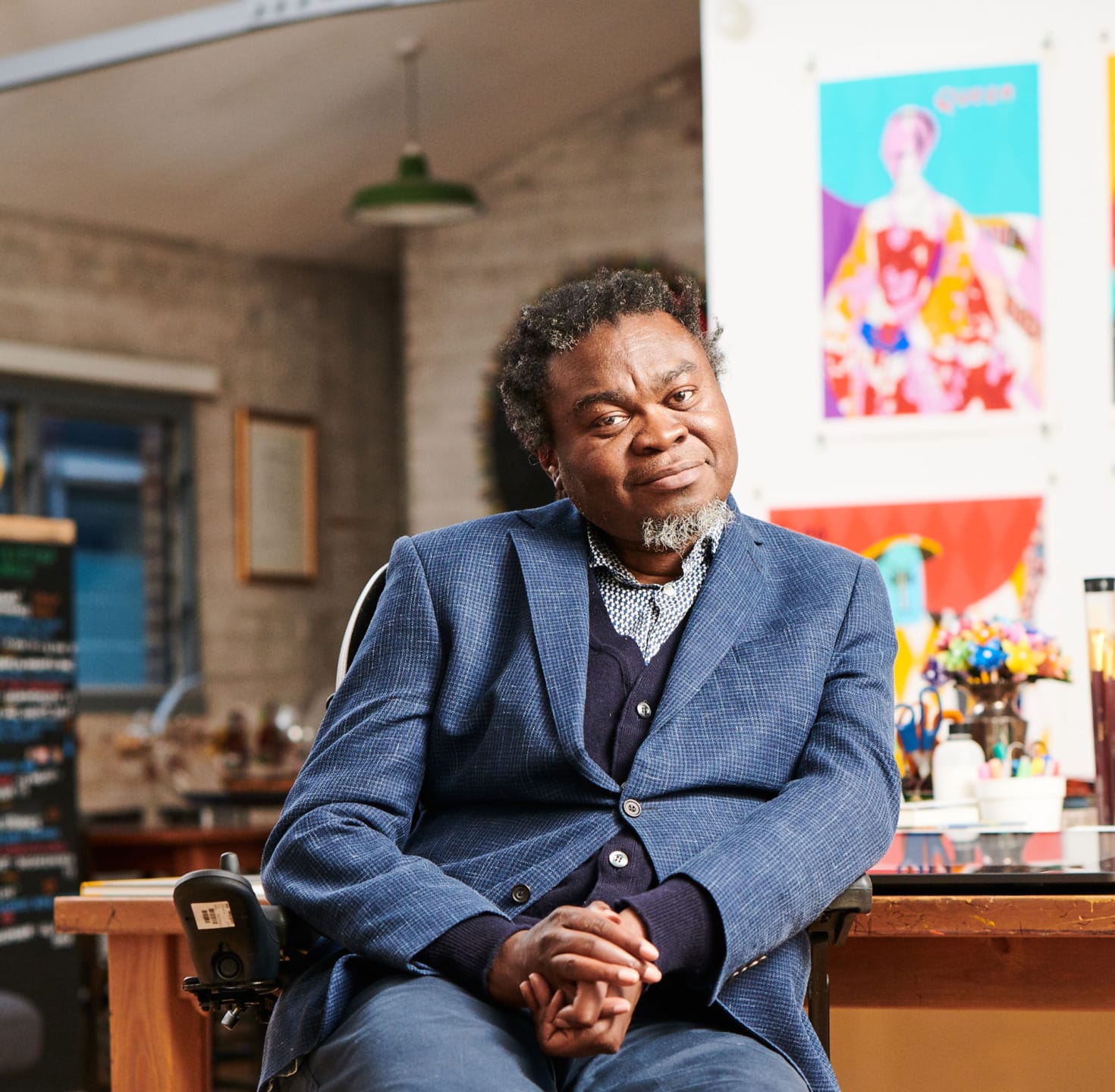 Man sitting at a desk in an art studio with colorful artwork on the walls behind him.