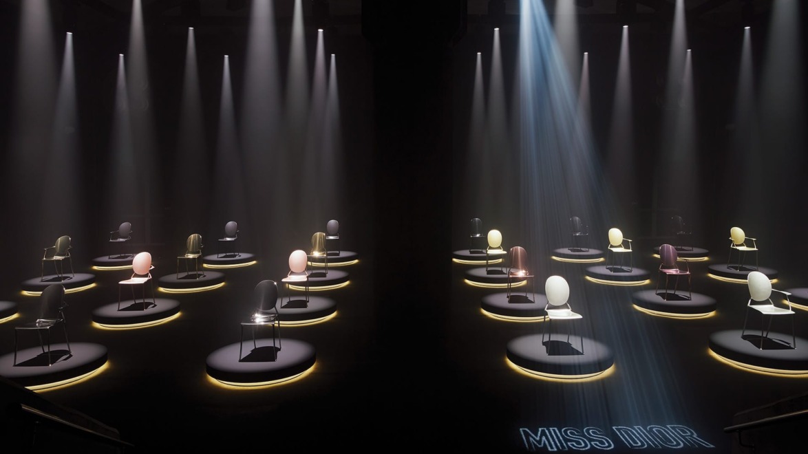 Illuminated chairs in a dimly lit room, each spotlighted in a circular display with "Miss Dior" projected on the floor.