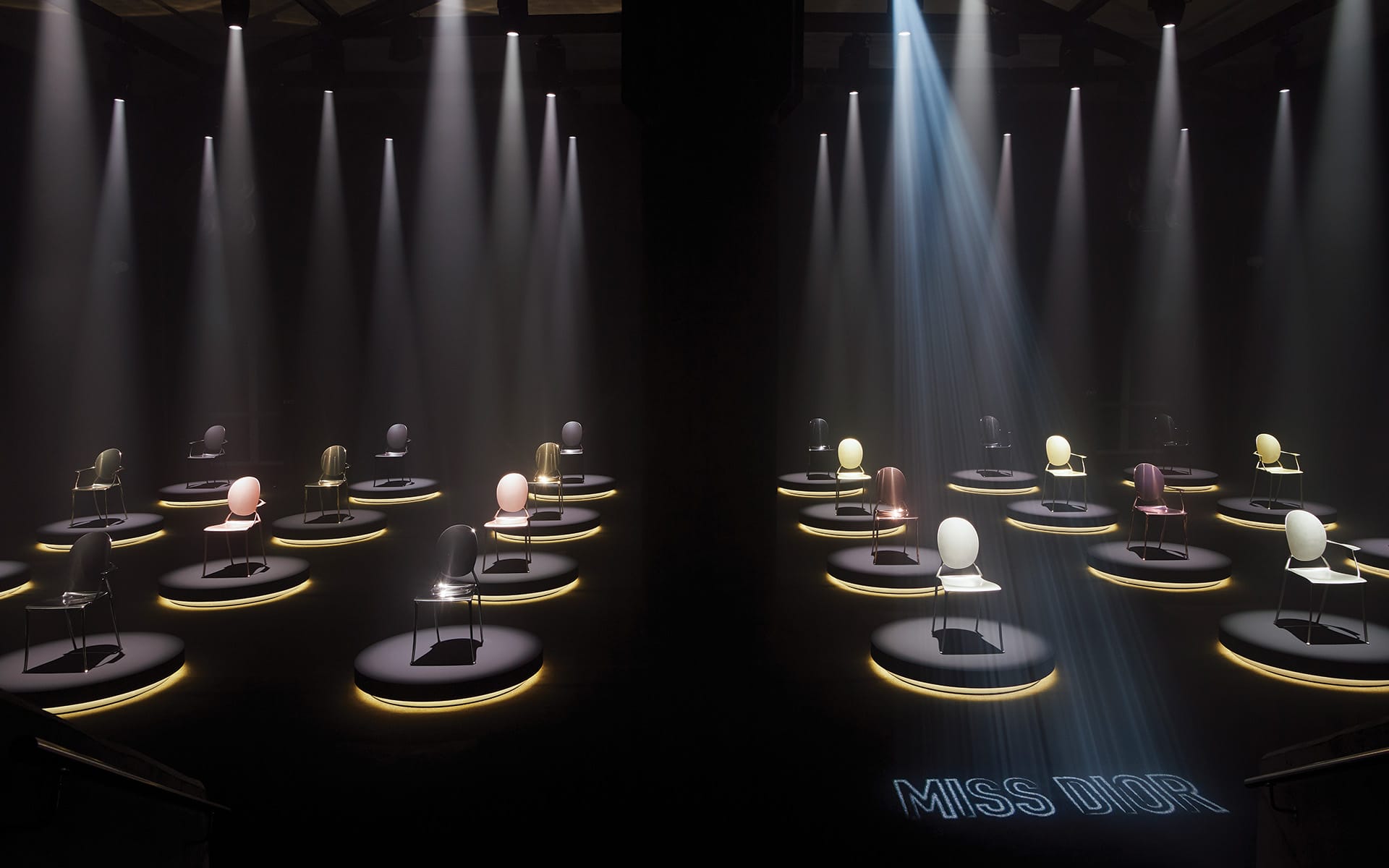 Illuminated chairs in a dimly lit room, each spotlighted in a circular display with "Miss Dior" projected on the floor.
