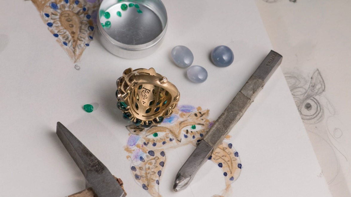 Jewelry design process with a ring, beads, hammer, and tools on a sketch of a jewelry piece.