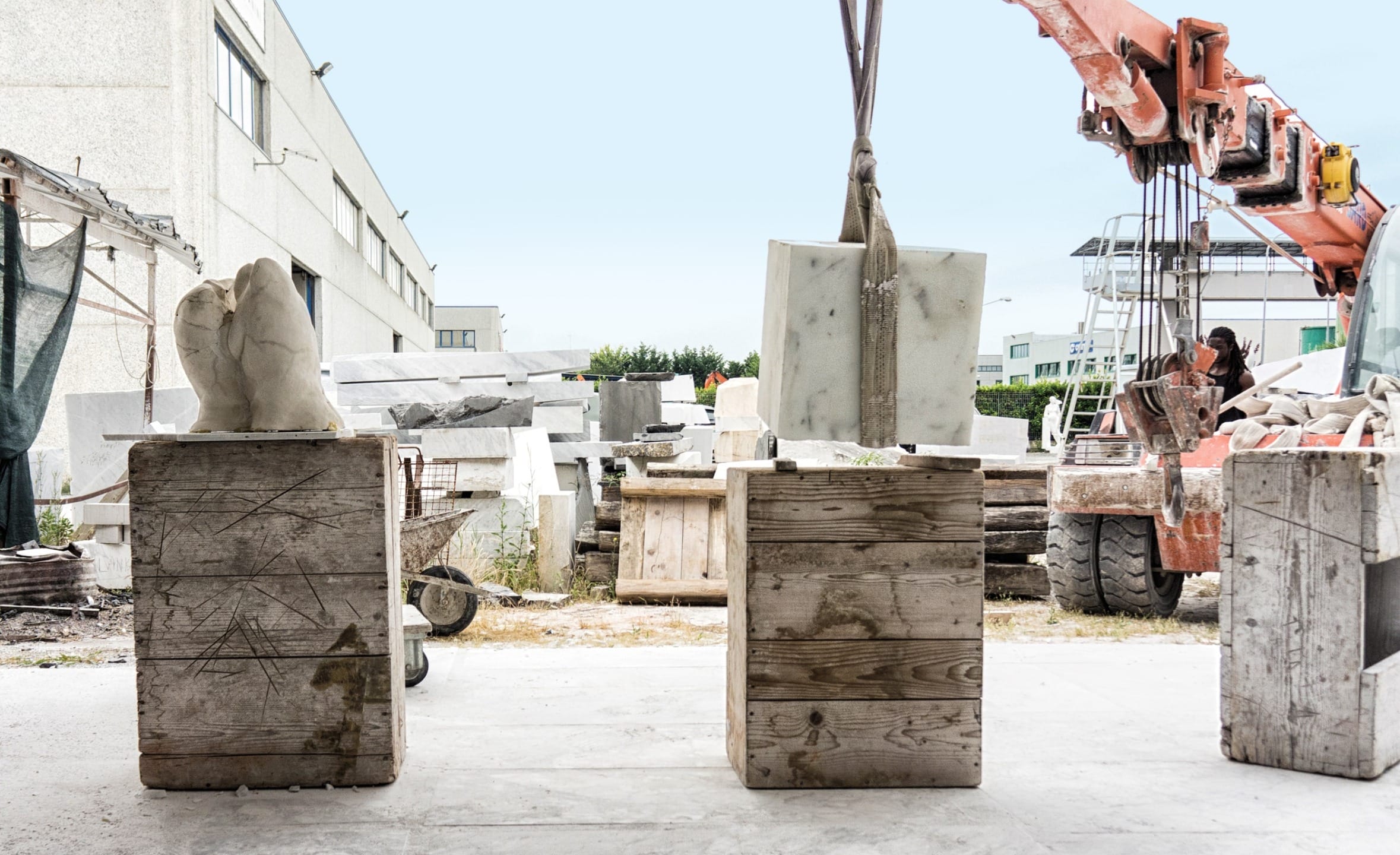 Stone sculpture and block in a workshop with crane and forklift in the background.