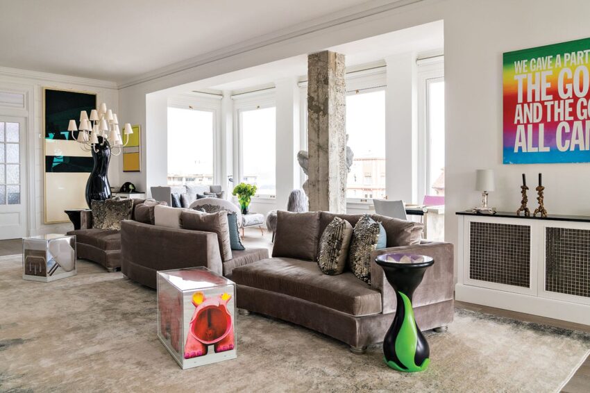 Modern living room with gray sofas, colorful artwork, large windows, and contemporary decor elements.