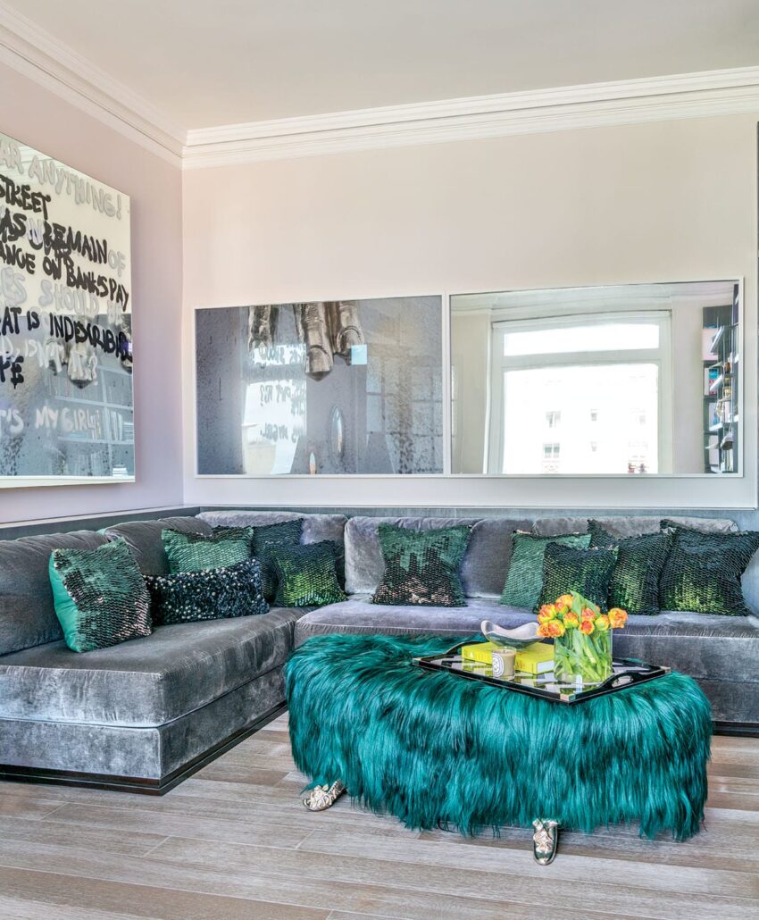 Stylish living room with gray sectional sofa, teal furry ottoman, decorative pillows, and contemporary wall art.