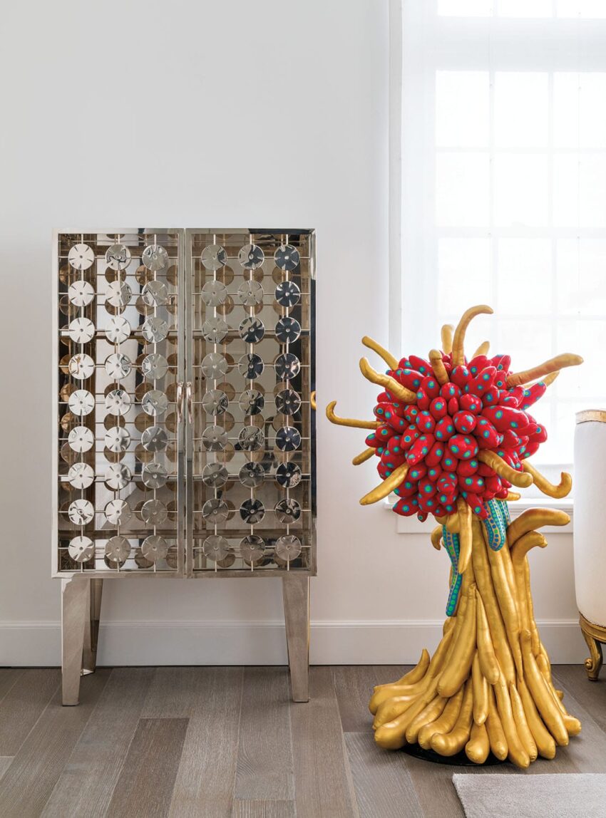 Decorative mirrored cabinet next to a colorful sculptural piece resembling abstract flowers in a modern interior setting.