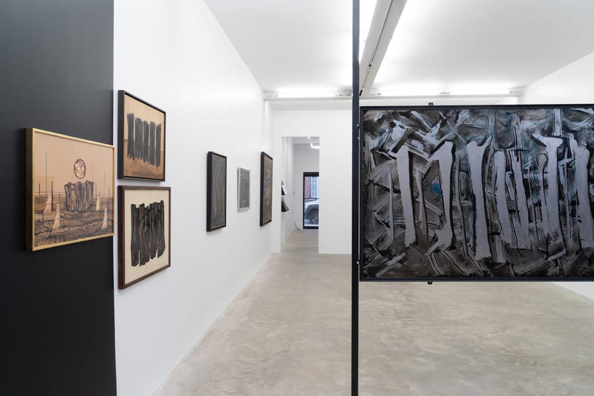 Art gallery interior showcasing modern abstract paintings with gray and black tones on white walls and concrete flooring.