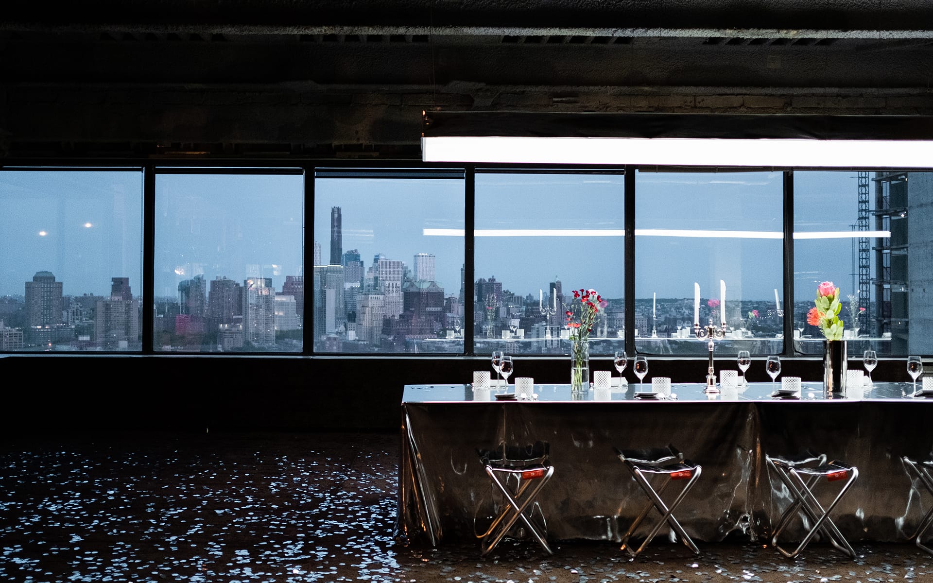 Elegant dining setup with glass table and chairs overlooking a cityscape through large windows, creating a luxurious ambiance.