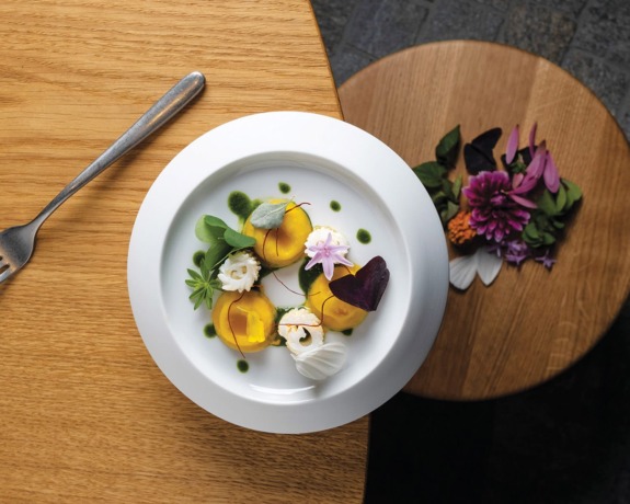 Gourmet dish with artfully arranged vegetables and edible flowers on wooden table with fork nearby.