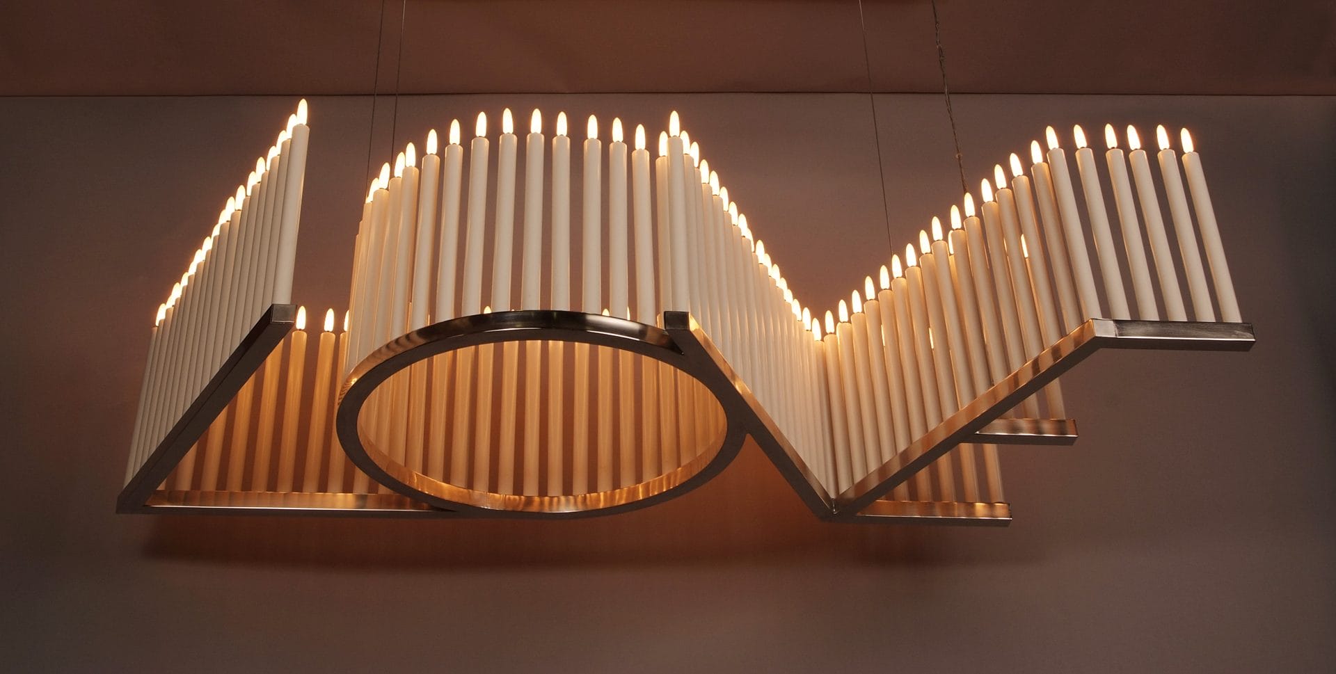 Modern chandelier with vertical LED tubes creating geometric shapes, hanging from the ceiling and illuminating warmly.