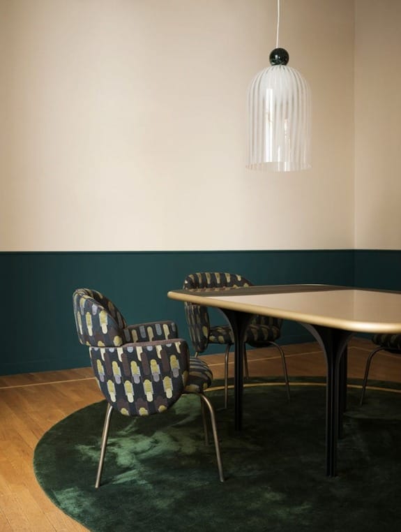 Modern dining room with a beige table, patterned chairs, green rug, and a hanging lamp.