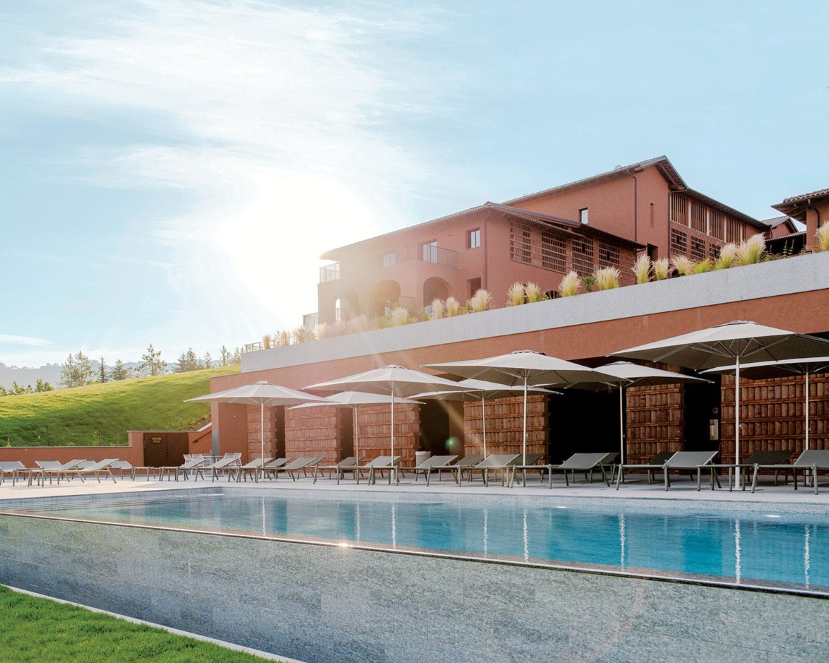 Luxury resort with outdoor pool, sun loungers, umbrellas, and modern architecture under a clear sky.