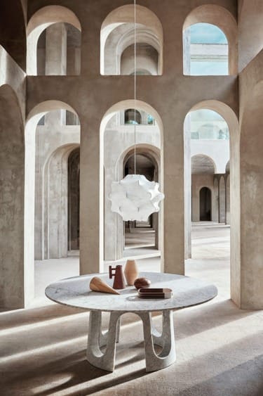 Modern interior with a round stone table, abstract centerpiece, and intricate archways creating a serene atmosphere.