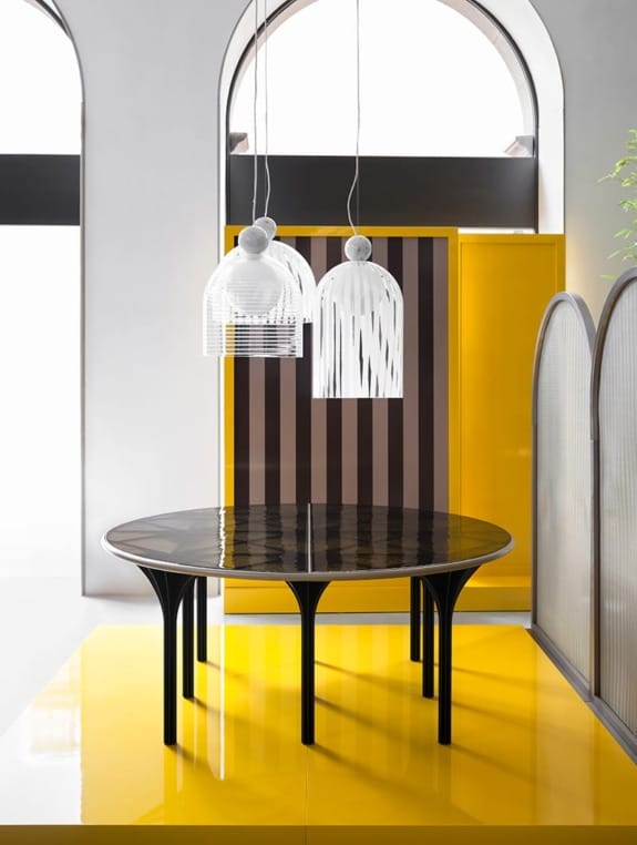 Modern dining room with a round black table, yellow accents, striped screen, and decorative pendant lights.
