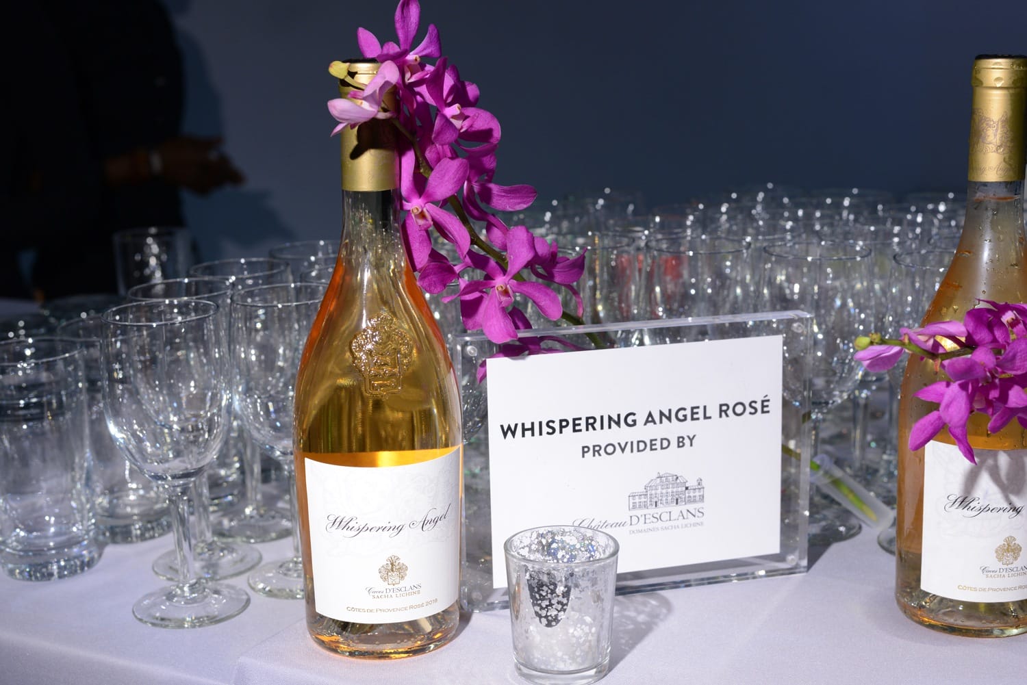 Bottles of Whispering Angel Rosé wine with glasses and floral decoration on a table.