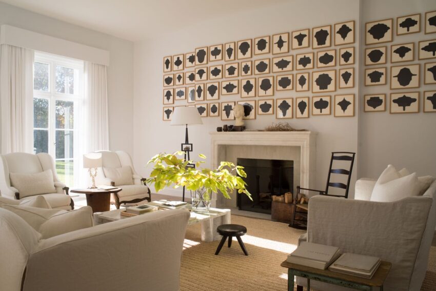 Elegant living room with white sofas, large window, and a wall of abstract art above a fireplace, centered around a green plant.