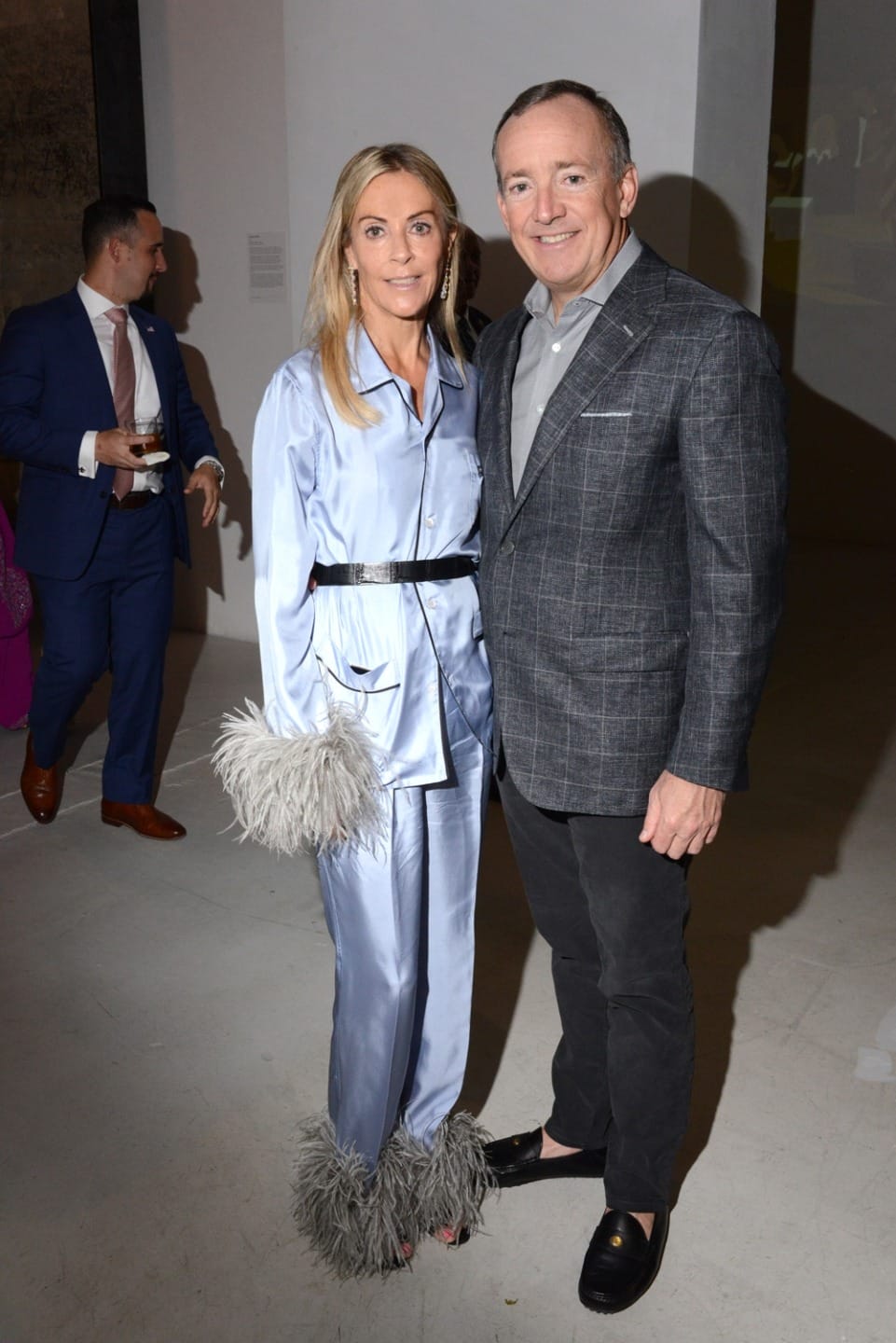 Two people posing together, one wearing a light blue outfit with feathered cuffs, and the other in a grey jacket and black pants.