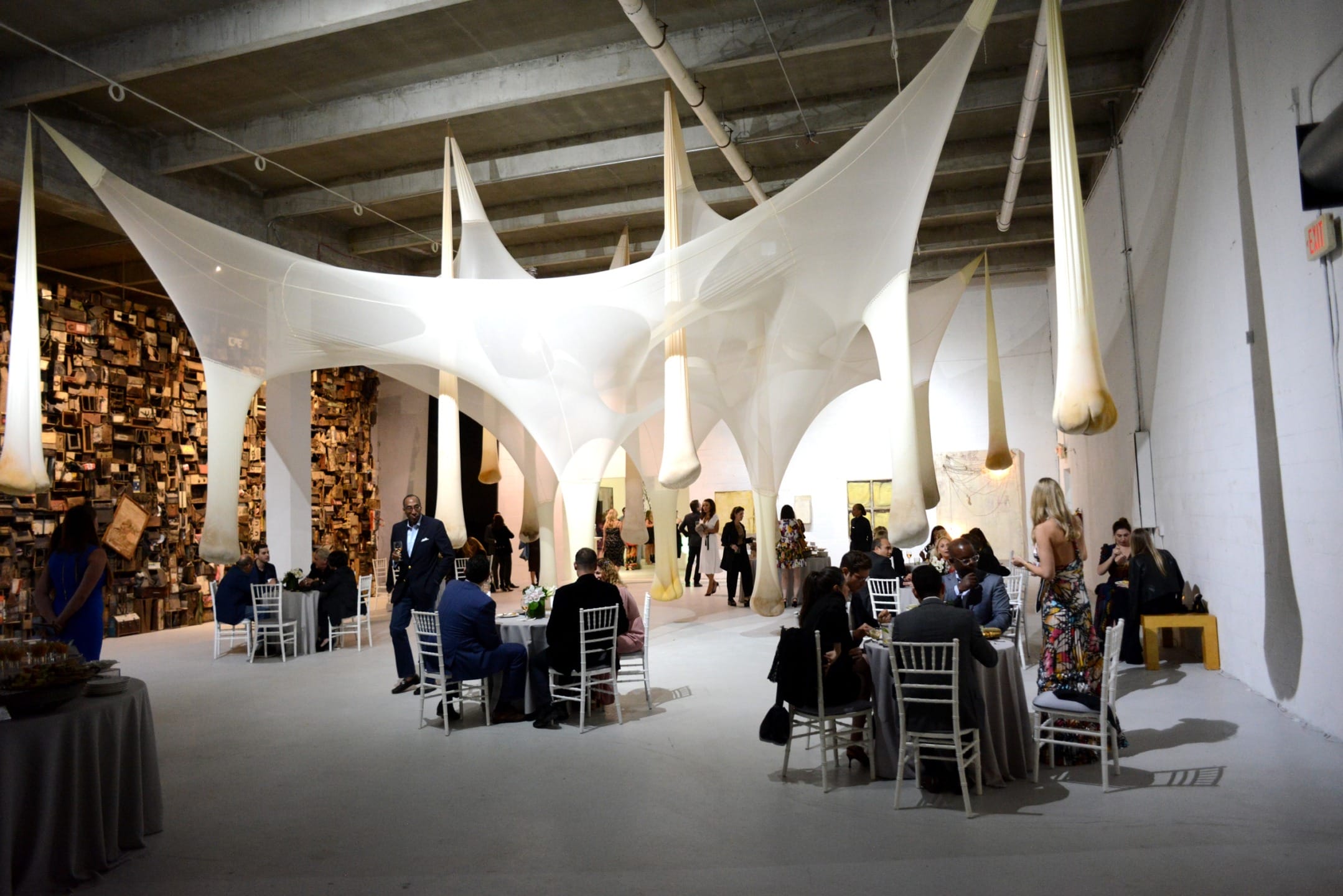 People dining at tables under large, artistic white fabric installations in a spacious, modern gallery setting.