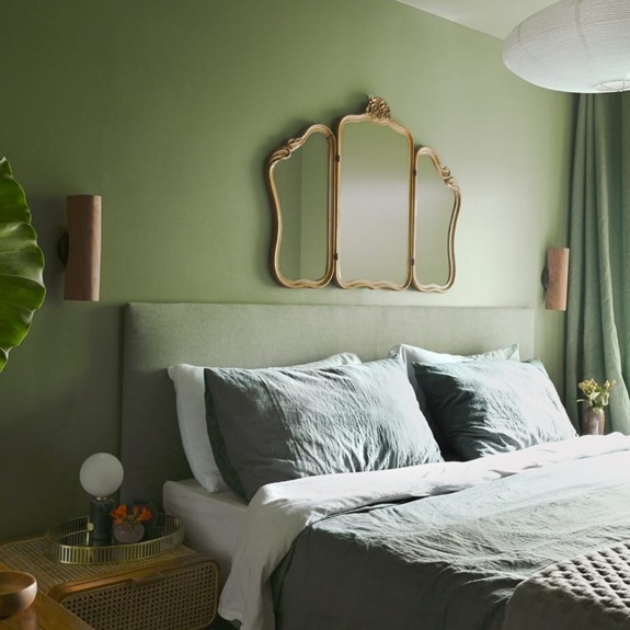 Cozy bedroom with green walls, modern furniture, and a large mirror above the bed.
