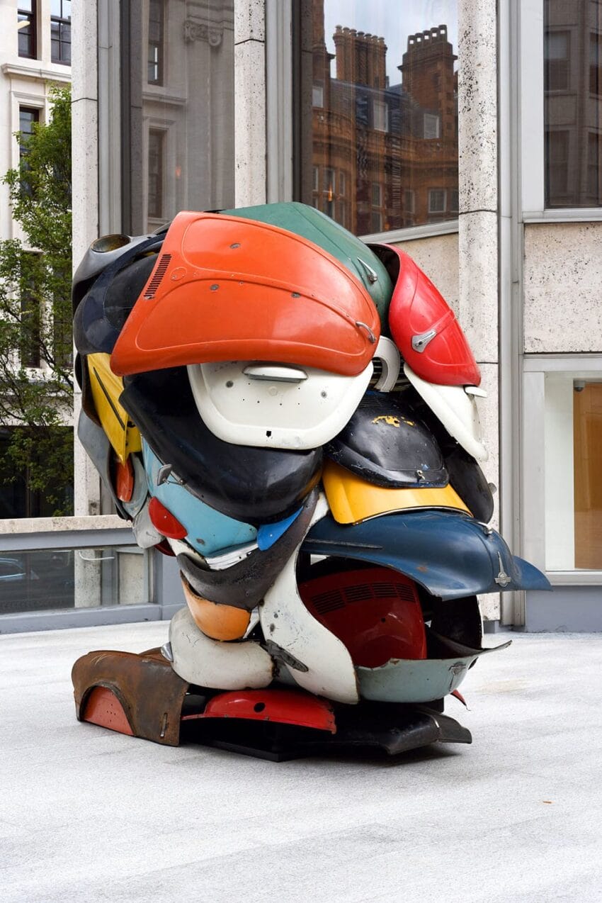 Colorful abstract sculpture made from stacked car parts displayed outdoors, featuring various shapes and textures.