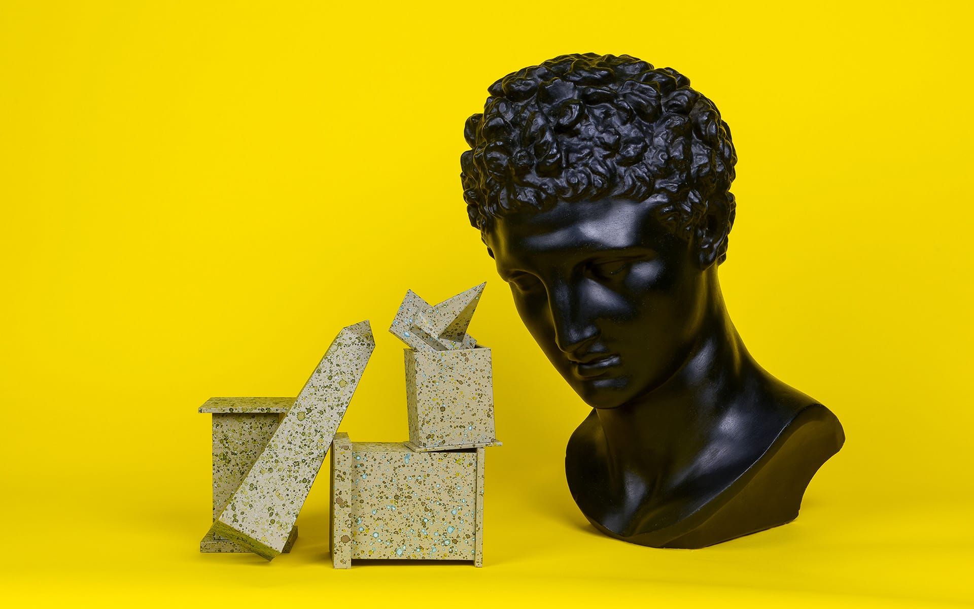 Black classical bust next to abstract geometric sculptures on a vibrant yellow background