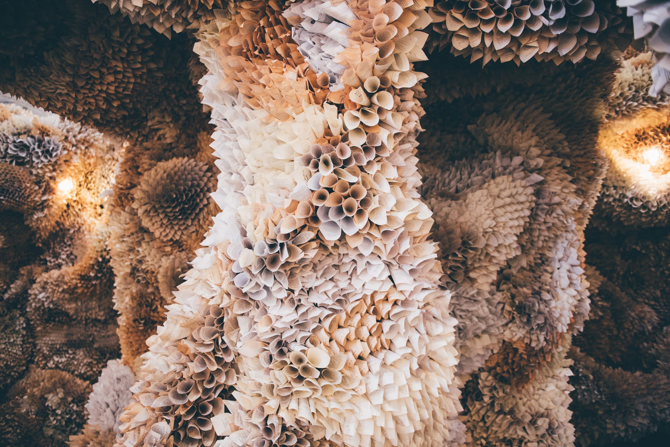 Intricate paper sculpture with layers of cone-shaped elements in beige and cream tones, creating a textured, artistic display.