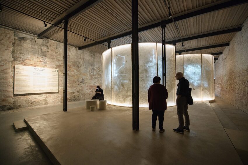 Visitors explore a dimly lit art installation with circular illuminated displays in a rustic gallery setting.